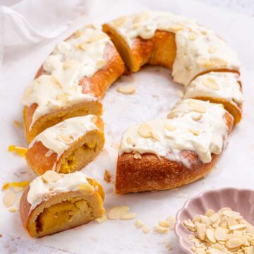 A keto pumpkin kringle danish is a pastry ring with a pumpkin cream filling, and cream cheese frosting with sliced almonds for garnish.