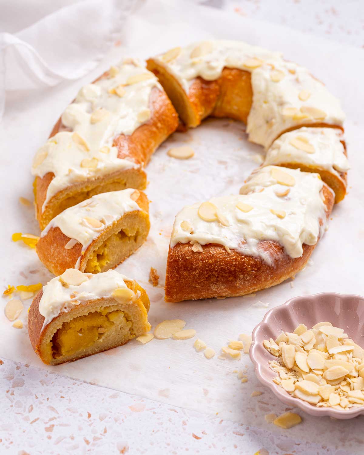 A keto pumpkin Kringle Danish is a  pastry ring with a pumpkin cream filling, and cream cheese frosting with sliced almonds for garnish.