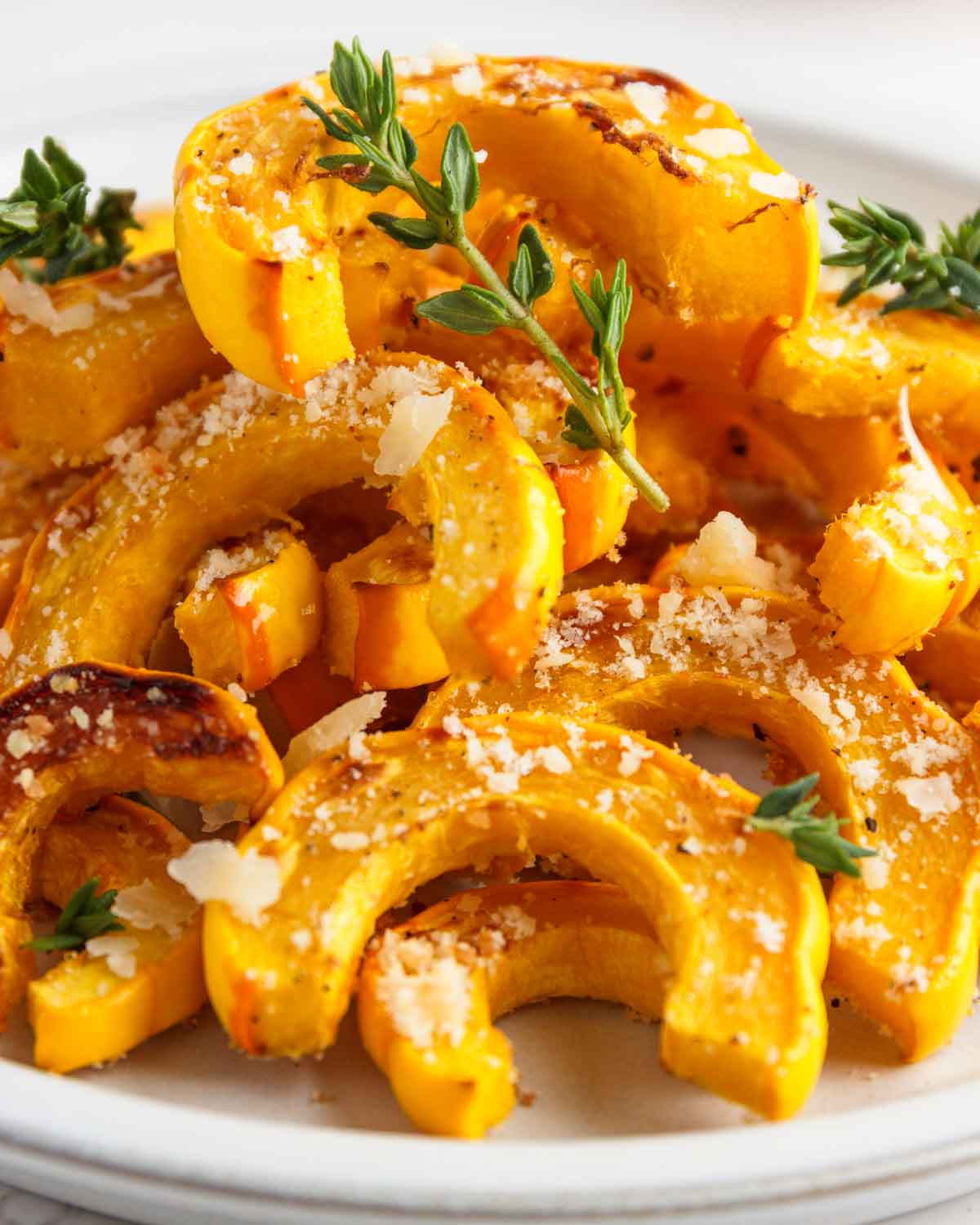 A plate of roasted parmesan delicata squash slices with thyme leaves.