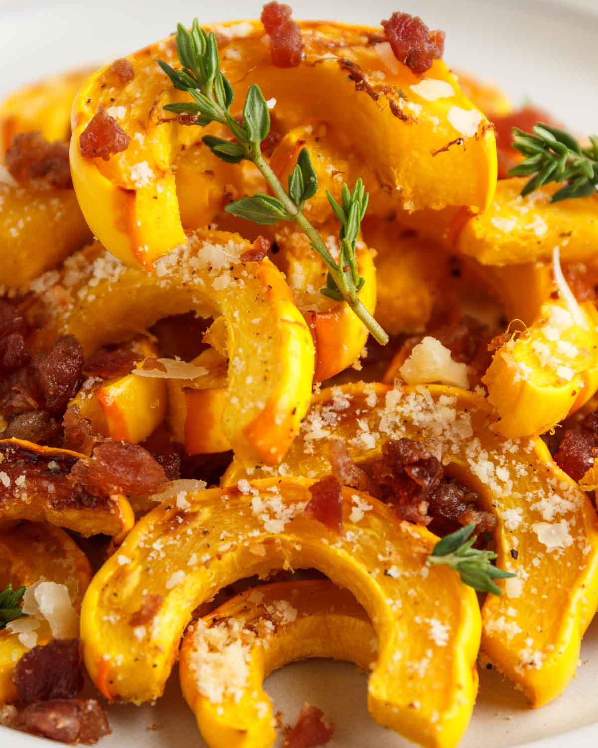 A plate of roasted parmesan delicata squash with thyme and bacon.