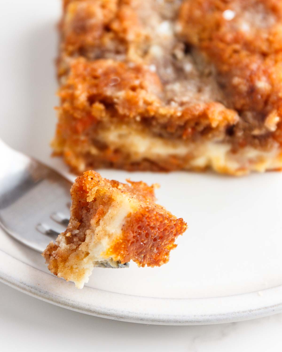 A bite of low carb carrot coffee cake with cream cheese on a fork on a plate.