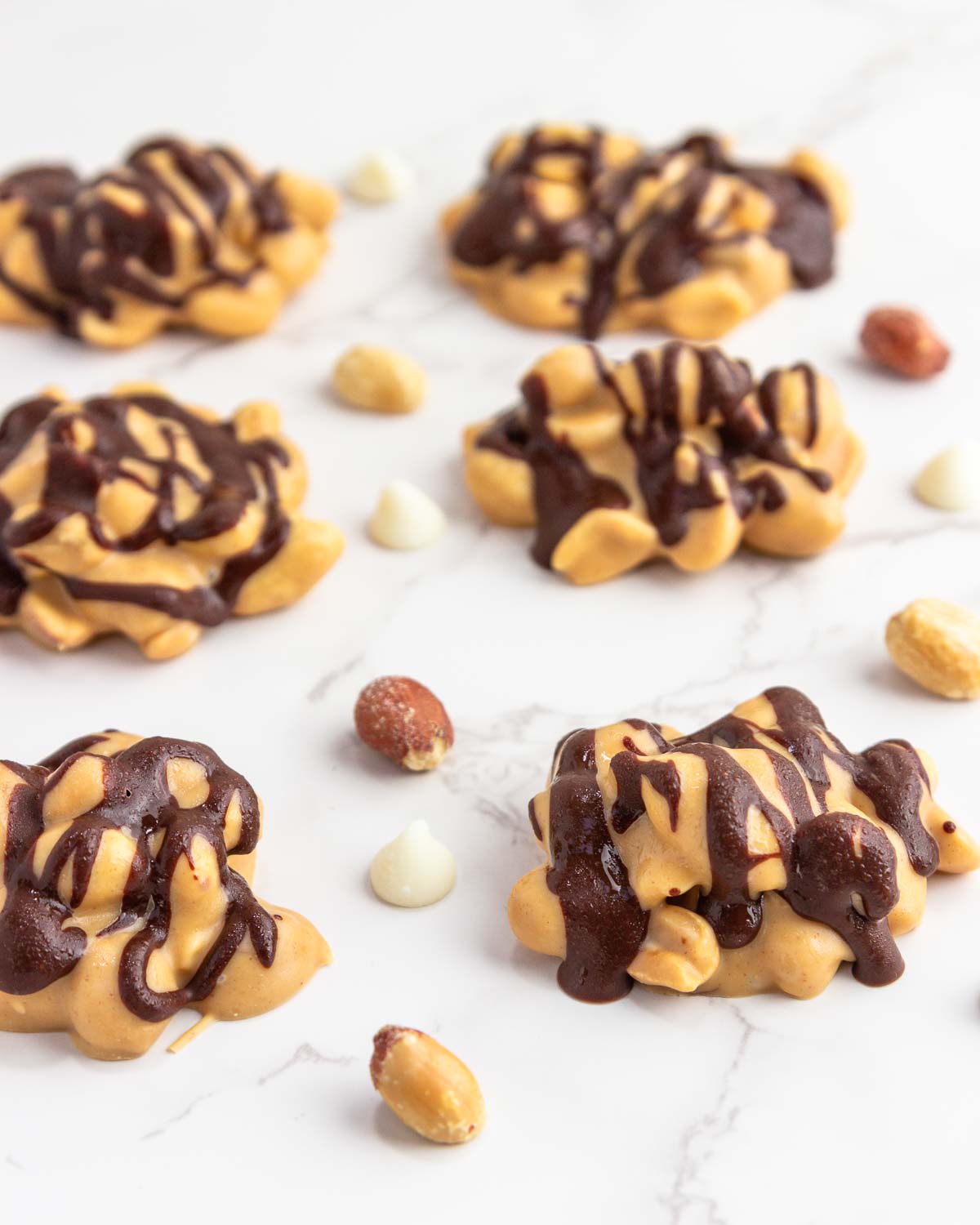 Snickers keto fat bombs are low-carb candy clusters on white marble background with scattered peanuts.