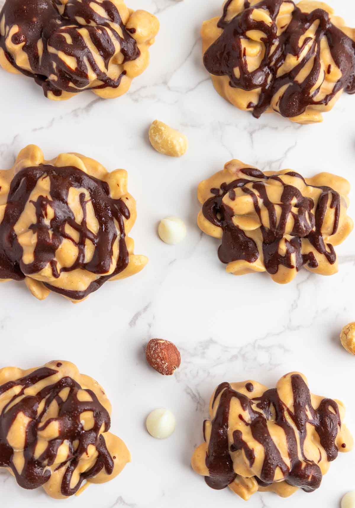 Snickers keto fat bombs are low-carb candy clusters on white marble background with scattered peanuts.