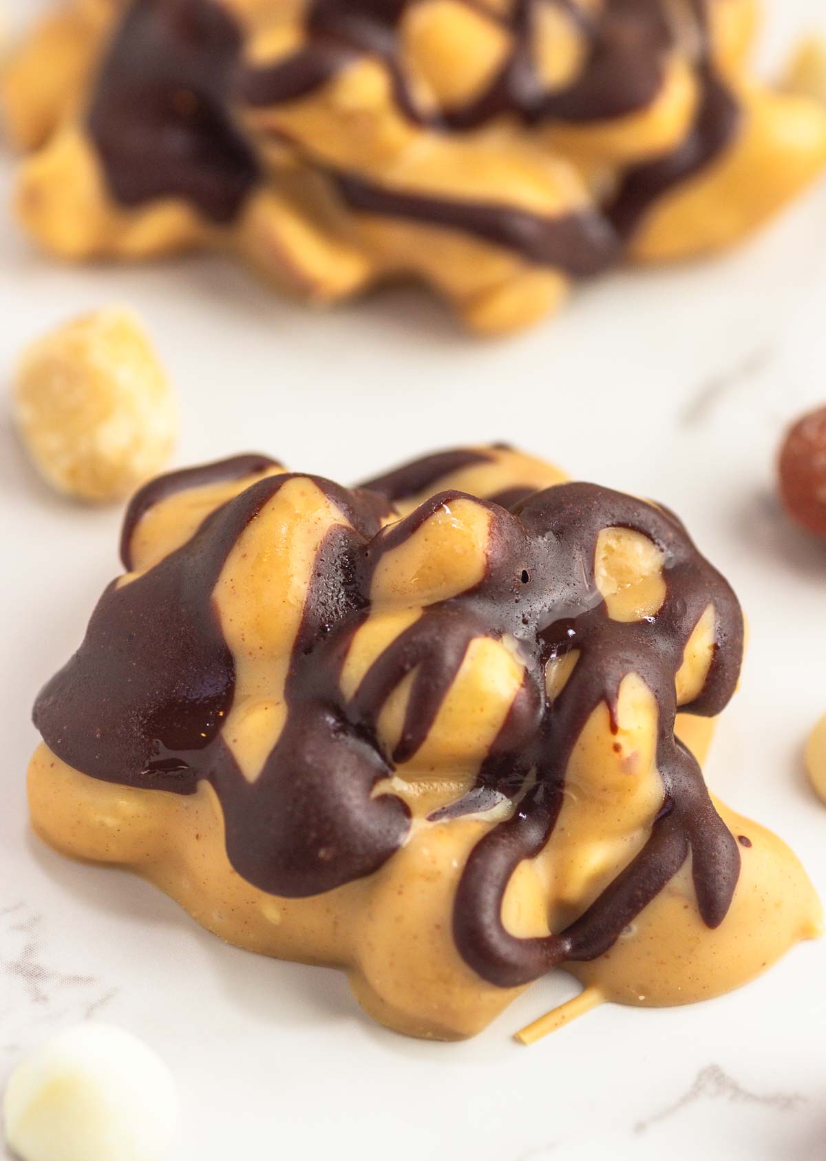 Two Snickers keto fat bombs candy clusters on white marble background with scattered peanuts.