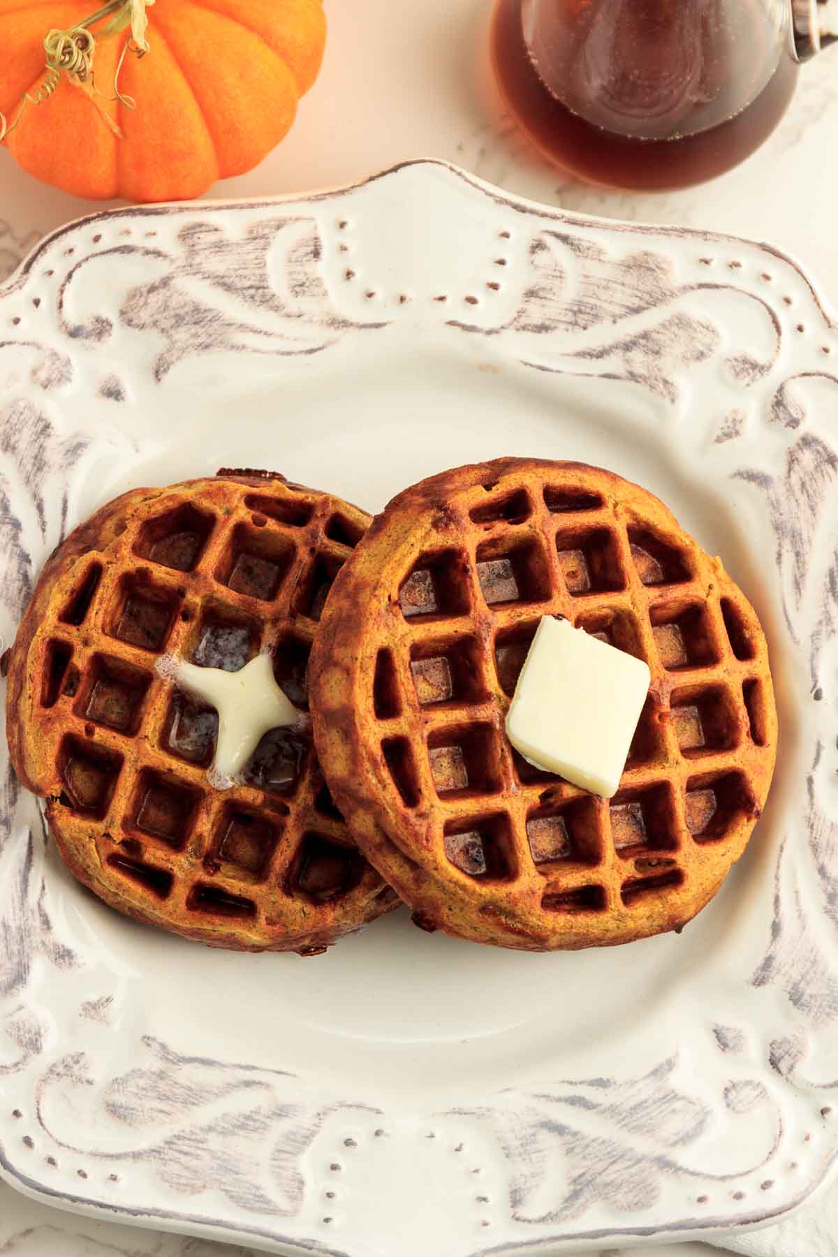 Two keto pumpkin spice waffles with butter and pumpkins in the background.