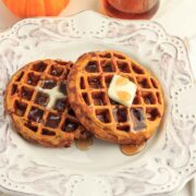 Two keto pumpkin spice waffles with syrup and pumpkins in the background.