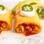 Two Chicken enchilada wraps topped with sour cream and jalapenos.