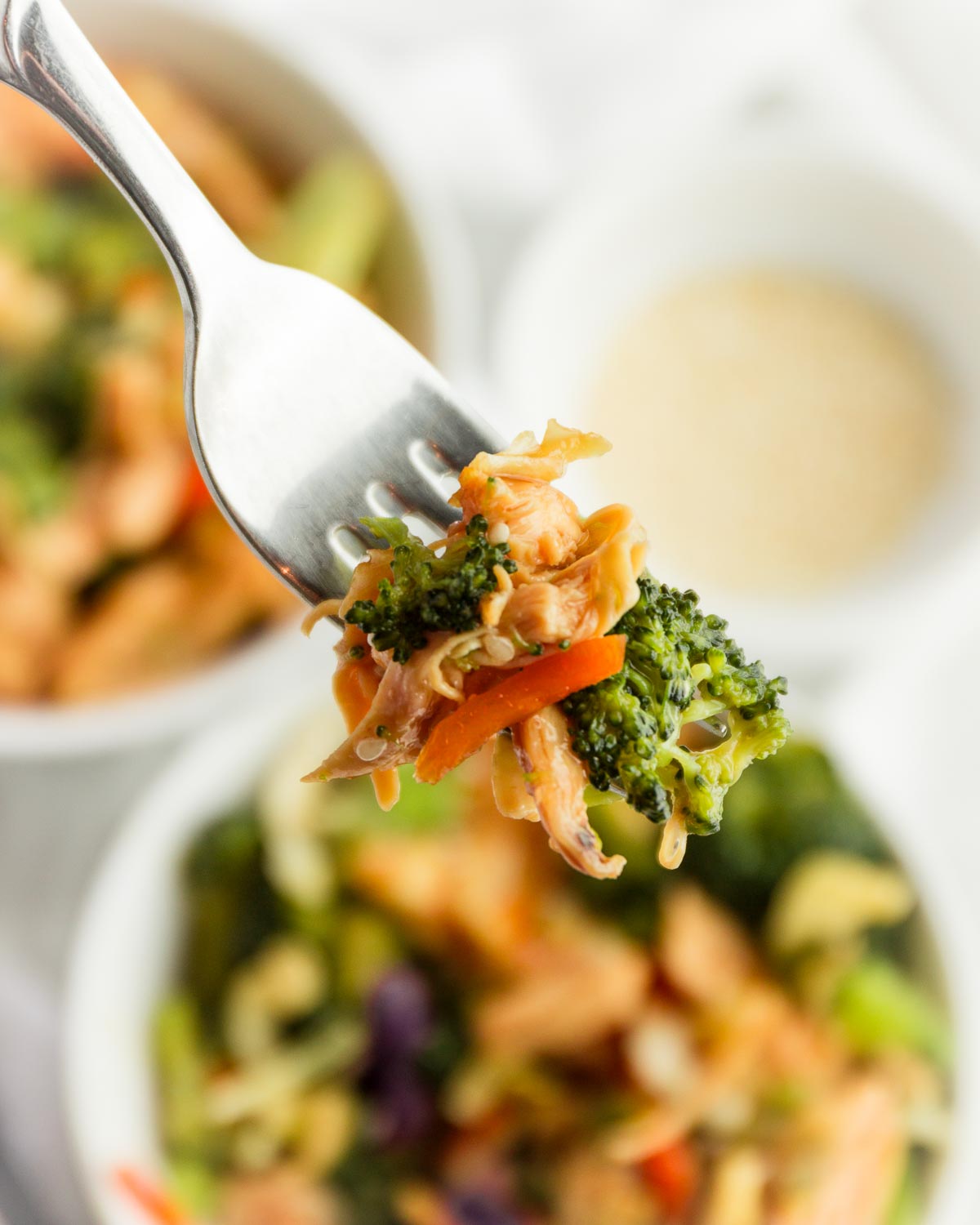 A fork holding a bite of keto chicken teriyaki stir fry with vegetables and cabbage.