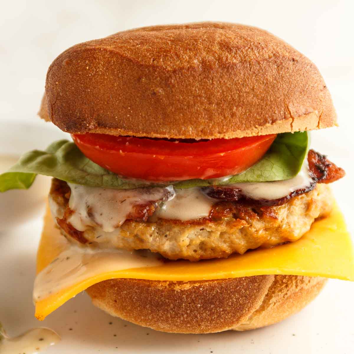 A cheddar ranch chicken burger with bacon, tomato, letttuce, ranch dressing, and pickles on a low-carb bun.