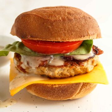 A cheddar ranch chicken burger with bacon, tomato, letttuce, ranch dressing, and pickles on a low-carb bun.