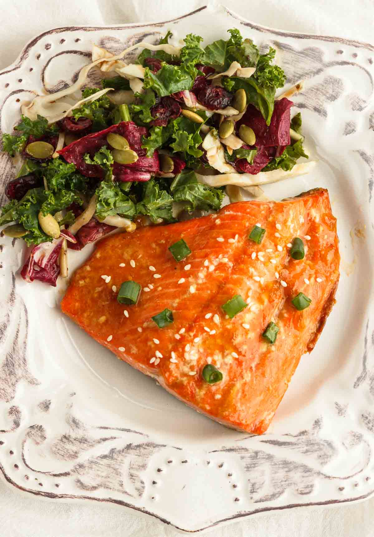Apricot glazed salmon served with a salad on a white plate.