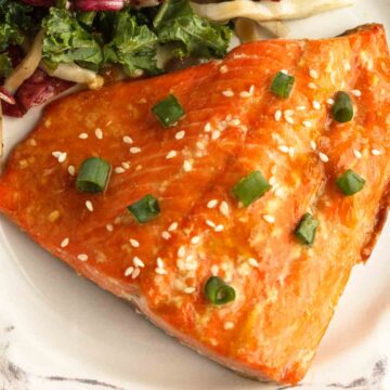 Apricot glazed salmon served with a salad on a white plate.