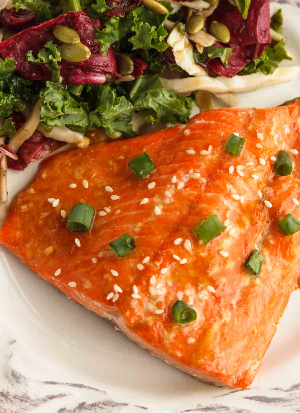 Apricot glazed salmon served with a salad on a white plate.