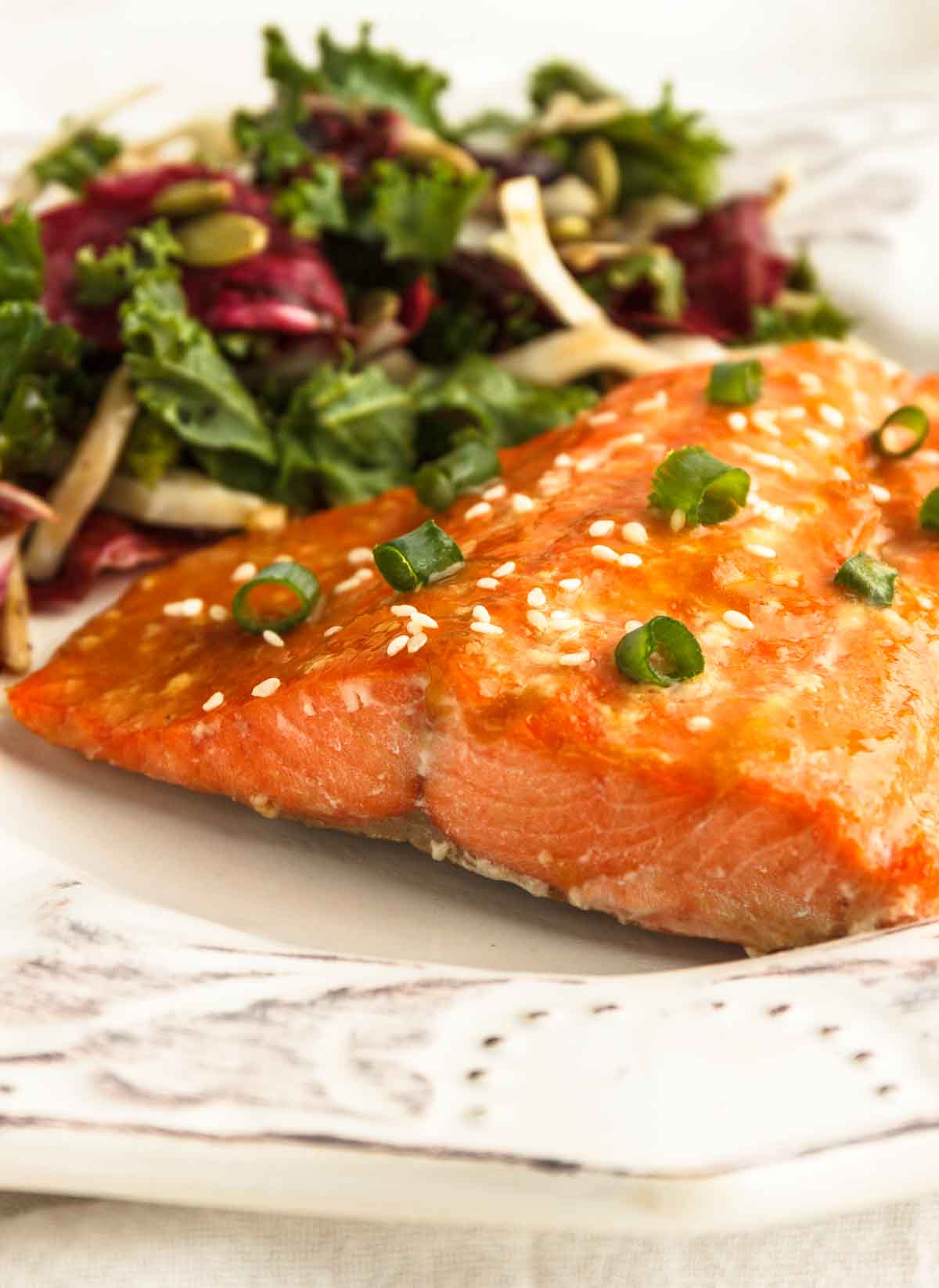 Apricot glazed salmon served with a salad on a white plate.