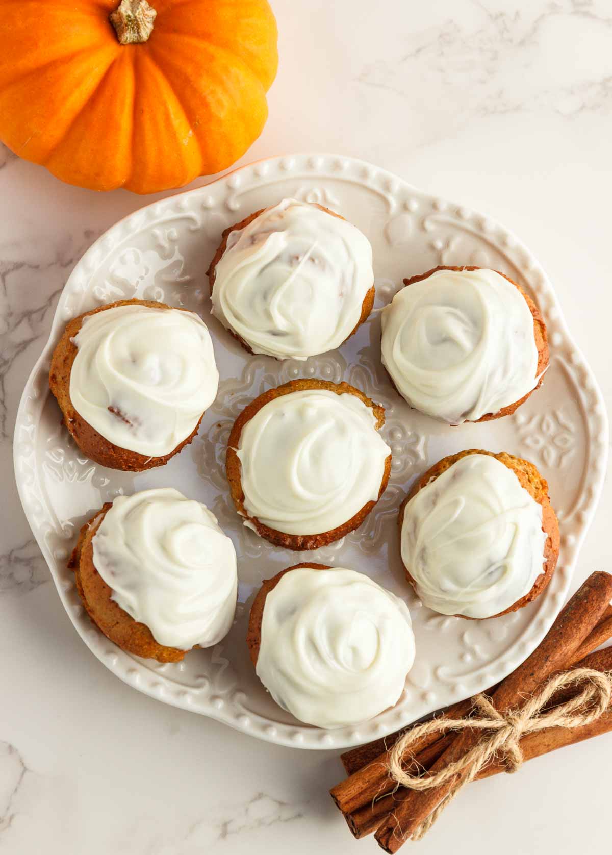 Pumpkin donut holes with white chocolate frosting on a white plate.