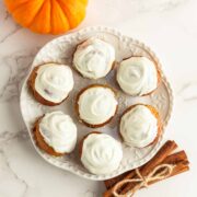 Keto pumpkin donut holes with white chocolate frosting on a white plate.