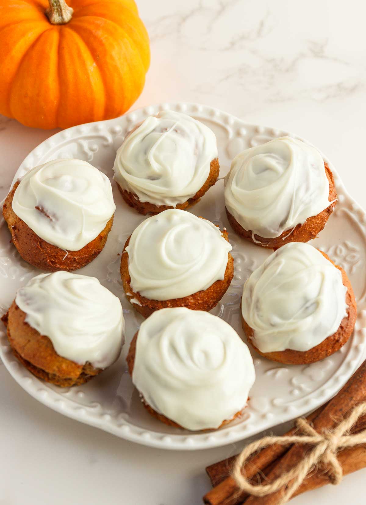 Pumpkin donut holes with white chocolate frosting on a white plate.