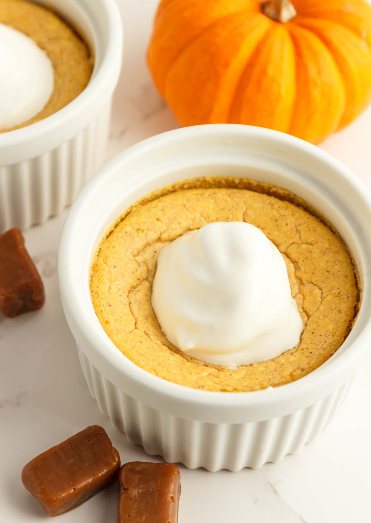 Two easy keto pumpkin cheesecakes in white ramekins with whipped cream.