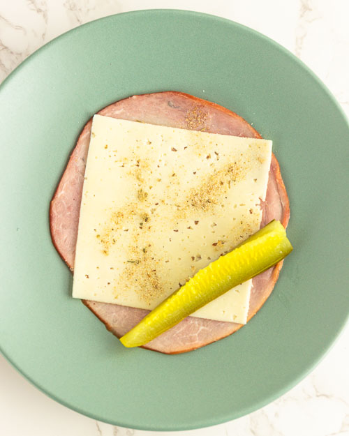 Adding a pickle spear to the ham and cheese slices..