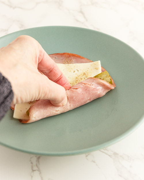 Rolling up the ham and cheese over the pickle.