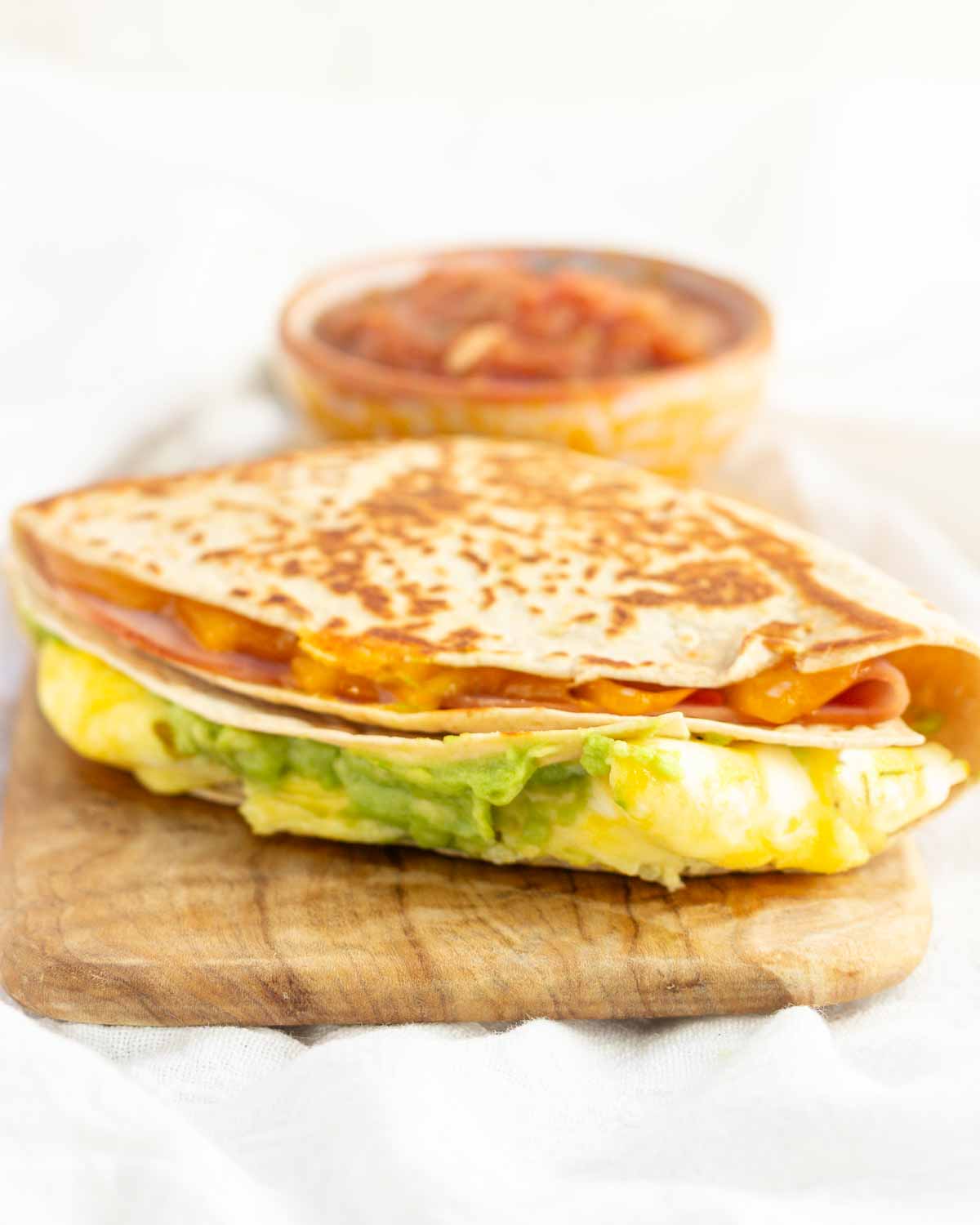 A breakfast tortilla wrap stacked with egg, cheese, ham, and avocado.