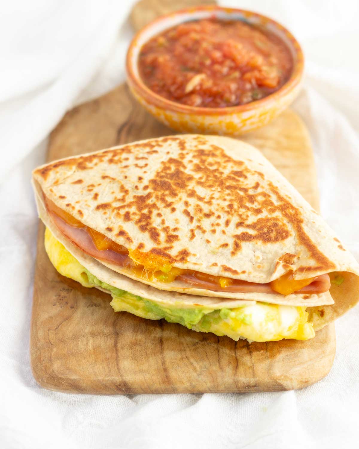 A breakfast tortilla wrap stacked with egg, cheese, ham, and avocado.