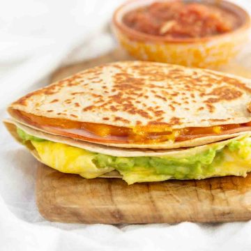 A breakfast tortilla wrap stacked with egg, cheese, ham, and avocado.
