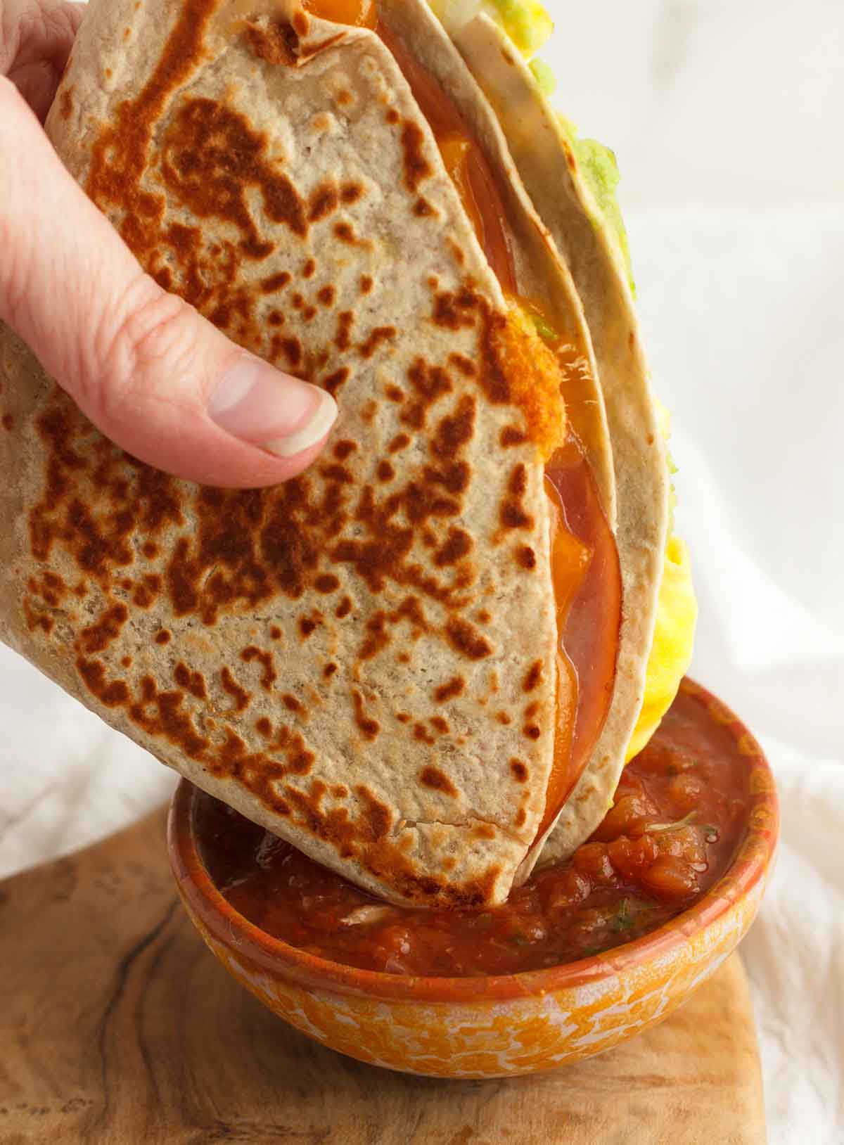 Dipping breakfast tortilla wraps in a bowl of salsa.