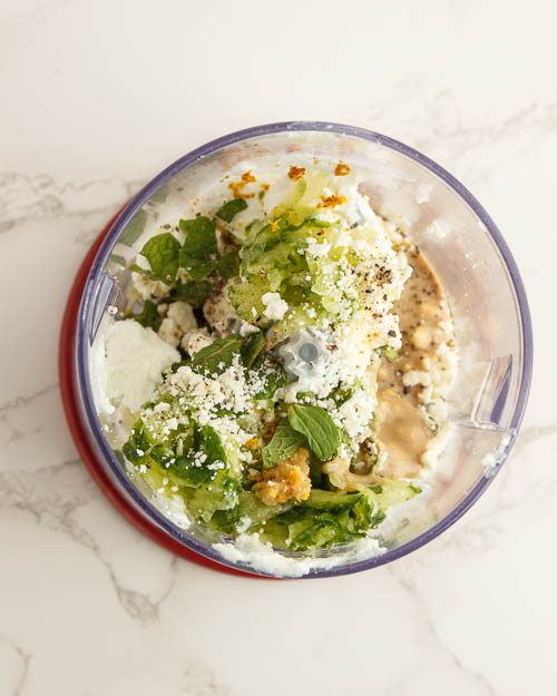 Adding the ingredients to make tzatziki sauce to a food processor.